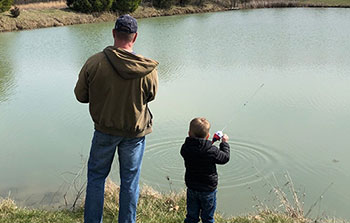 Father fishing at pond with young son